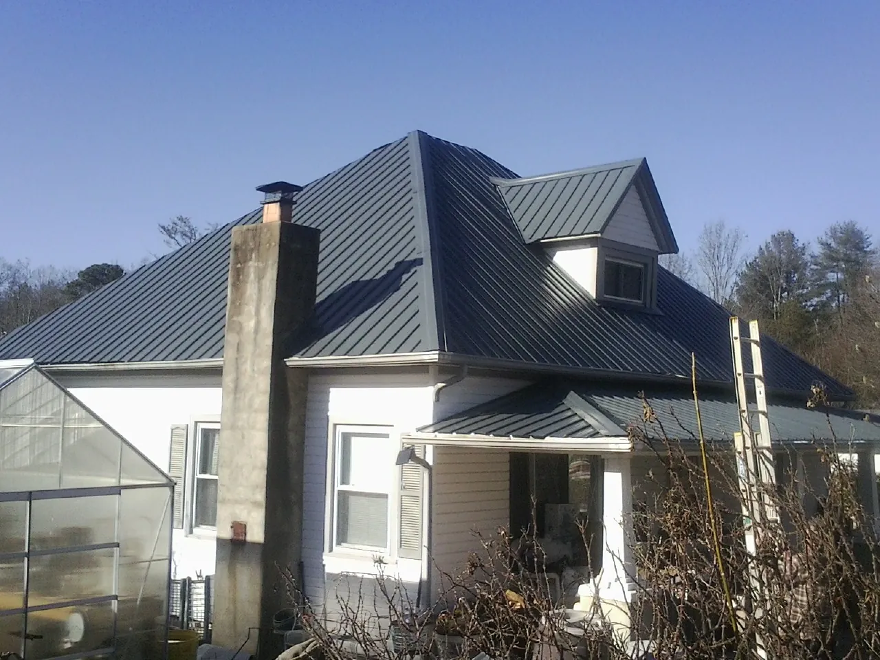 Dark blue standing seam metal roof on a white farmhouse with dormer — Slate & Tile Roof Repair by Roofing Brothers in Linton