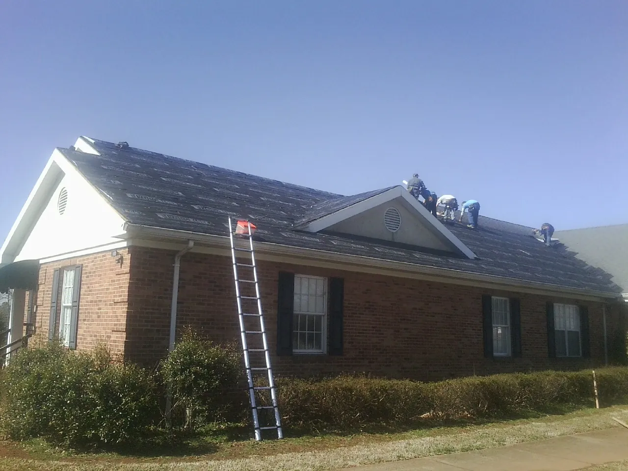 Crew tearing shingles off a brick ranch roof with a ladder set — Emergency Roof Repair work by our crew in Linton