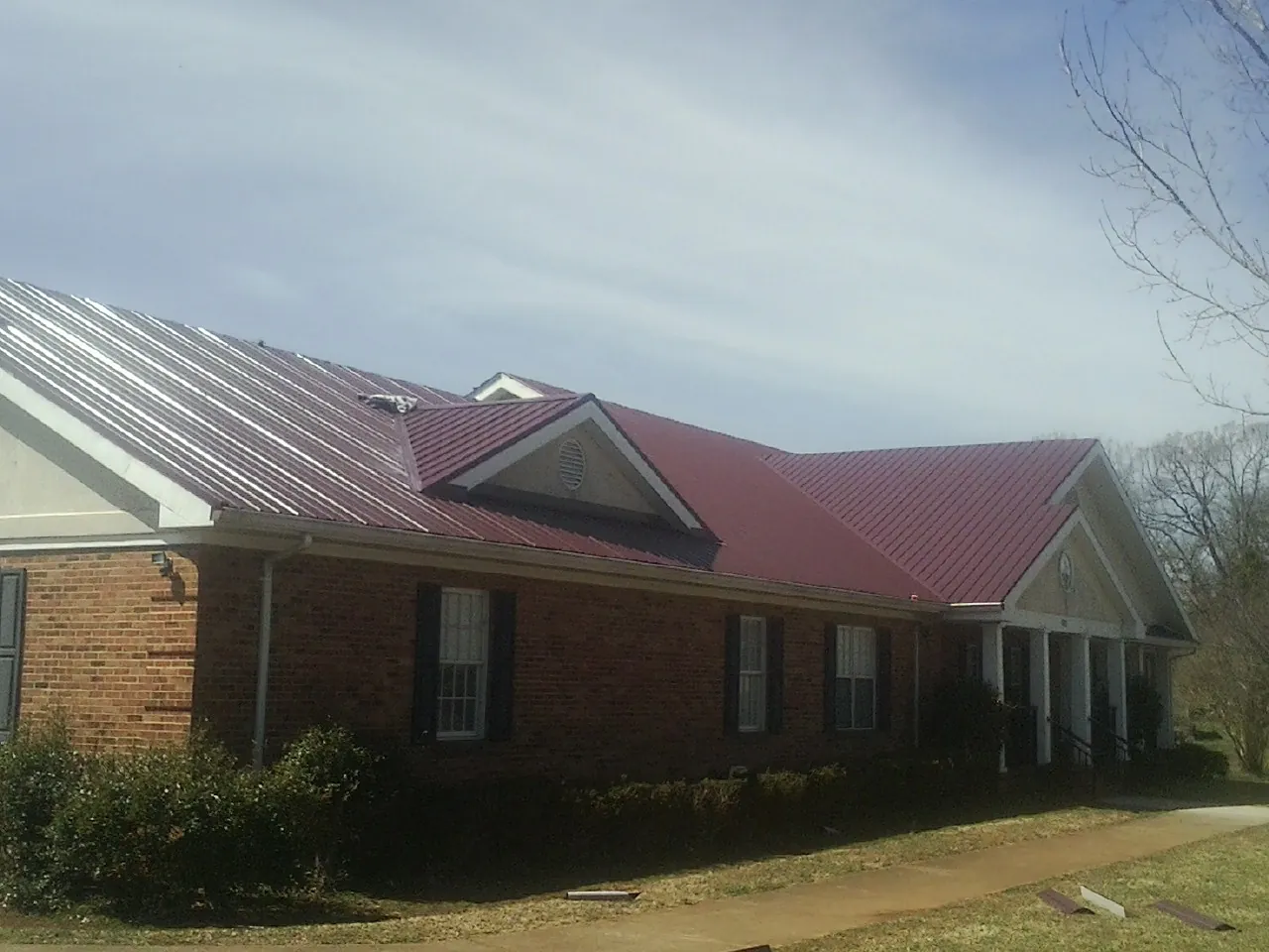 Red metal roof with gabled entries on a long brick building, from a Hail Damage Roof Repair job in Linton