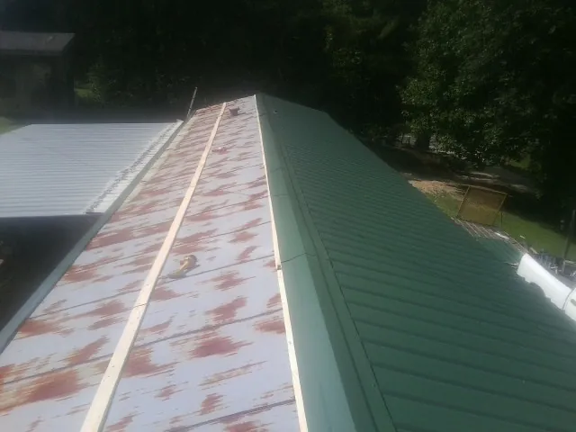 Old rusted panels beside newly installed green metal roofing — Wind Damage Roof Repair by Roofing Brothers in Linton
