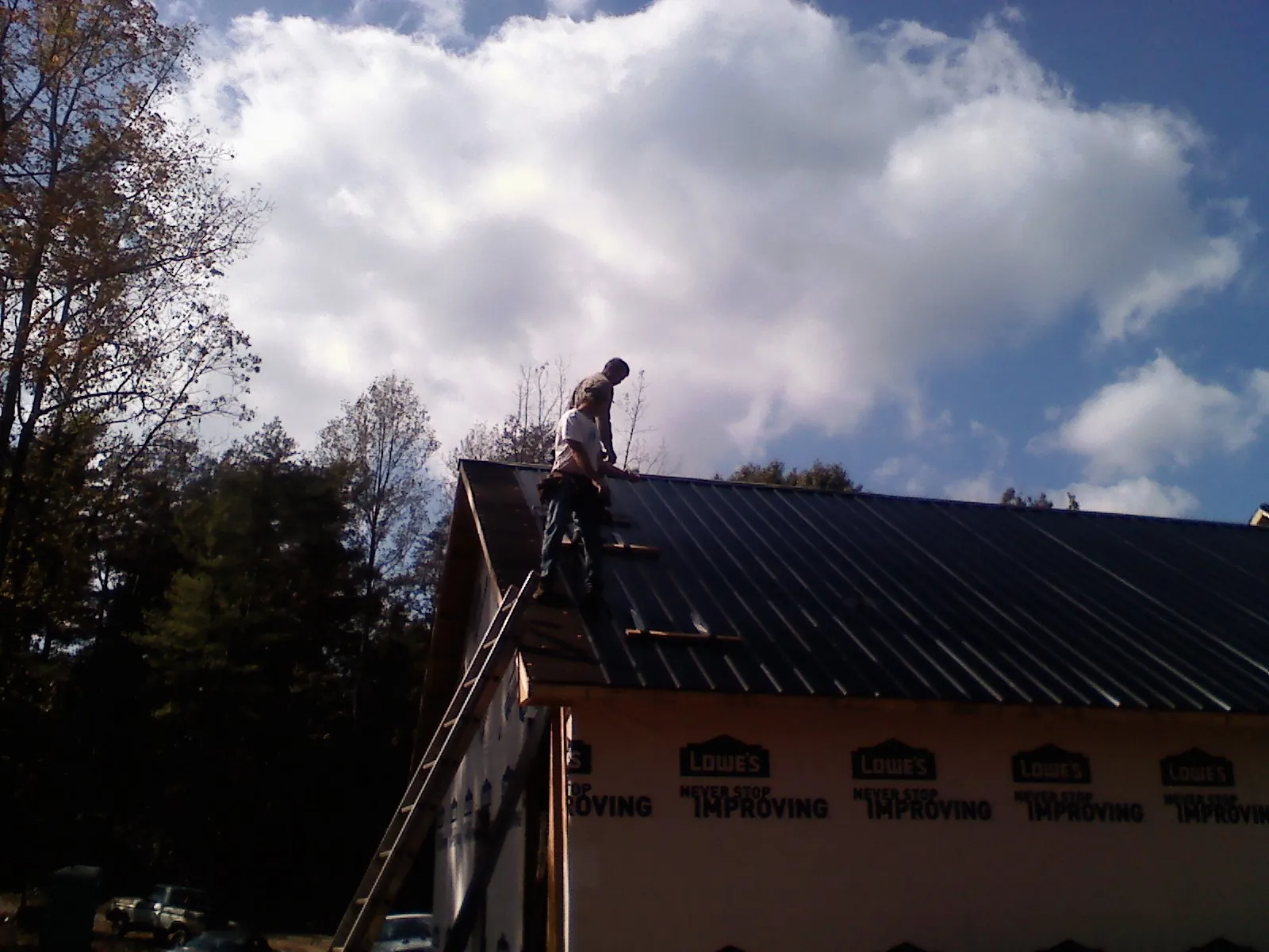 Roofer fastening dark metal panels high against a cloudy sky, from a Roof Inspection job in Linton