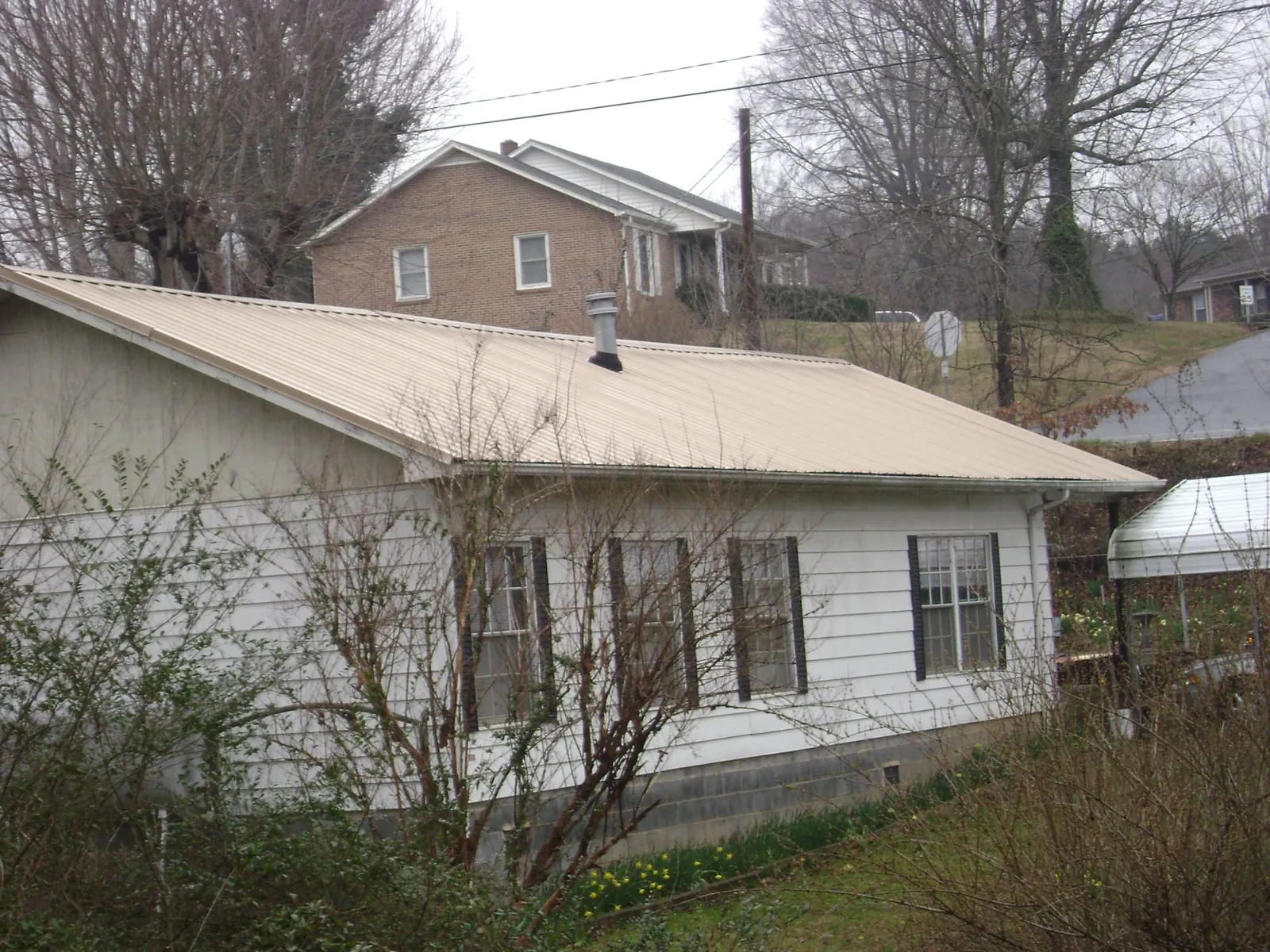 Tan metal roof on a white sided house set into a hillside — Commercial Roofing by Roofing Brothers in Linton