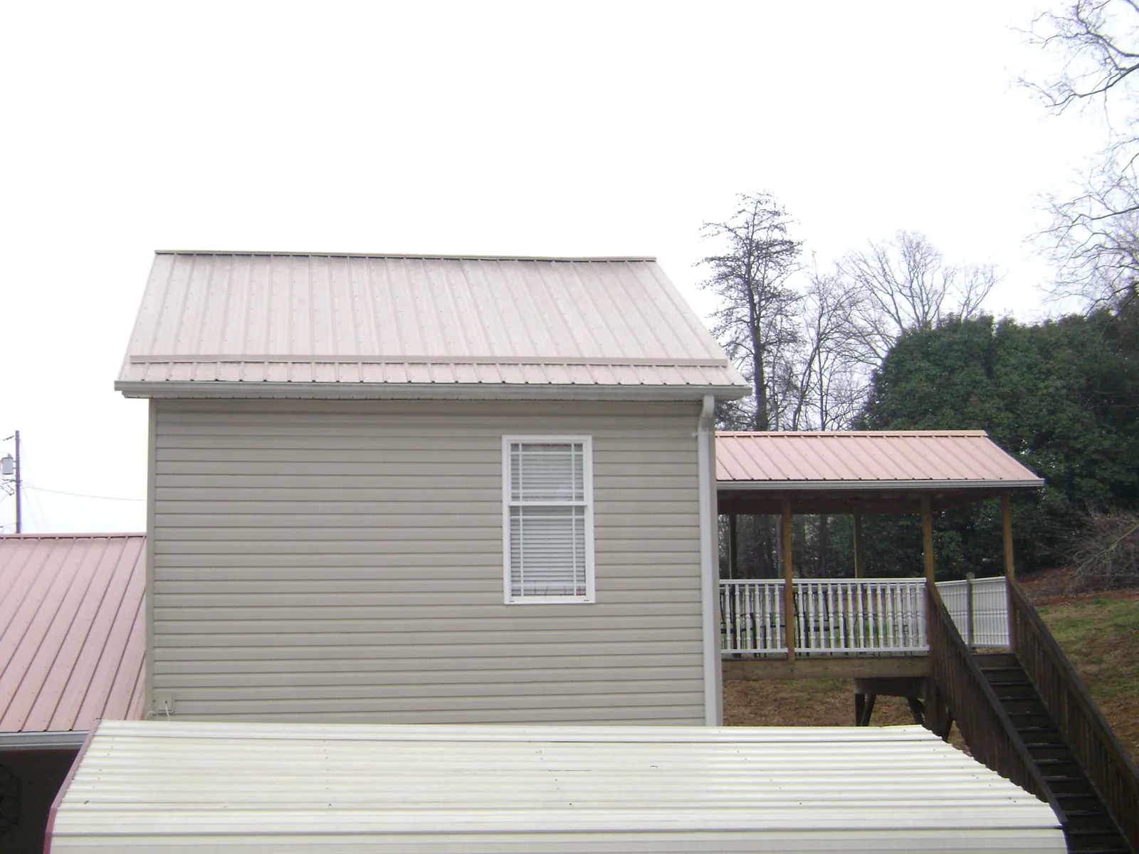 Tan metal roofs on a two story addition and attached porch, from a Roof Replacement job in Linton